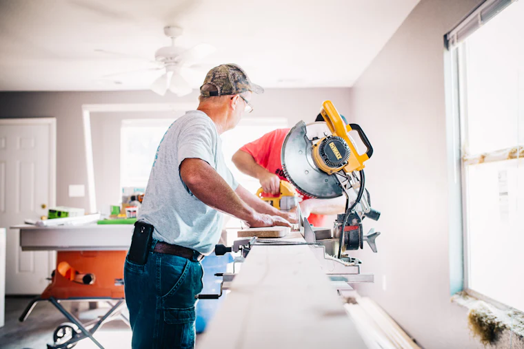 Stock photograph: a carpenter cutting trim on a mitre saw inside a finished room.